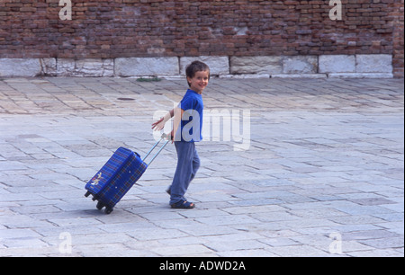 Ragazzo (6-7) tirando la valigia lungo il marciapiede Foto Stock