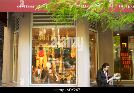 Scena di strada Chicago Illinois uomo indossare tuta sit banco quotidiano di lettura esterno esclusivo delle donne s negozio di abbigliamento Foto Stock