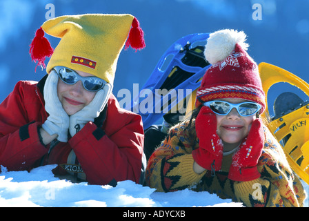 Le ragazze che giace nella neve, indossando occhiali da sole e tappi Foto Stock