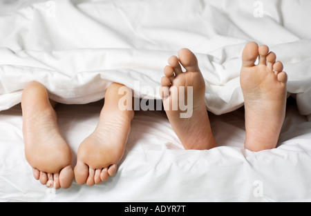 Coppia giacendo in letto, bassa sezione, close up dei piedi Foto Stock