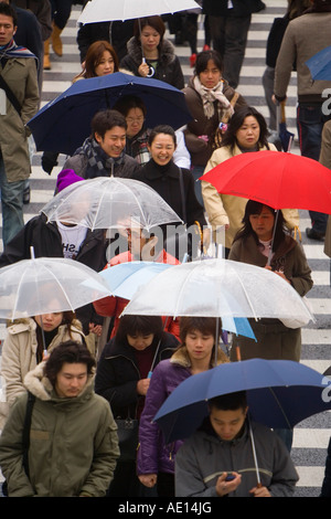 Asia Giappone Honshu Tokyo Shibuya pedoni che attraversano un incrocio occupato con ombrelloni in un giorno di pioggia Foto Stock