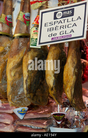 Appendere su garretti prosciutto cotto nel mercato coperto La Boqueria a La Rambla, Barcelona Spagna Foto Stock