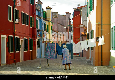 Una vecchia signora si blocca su una linea di servizio lavanderia contro case colorate Foto Stock