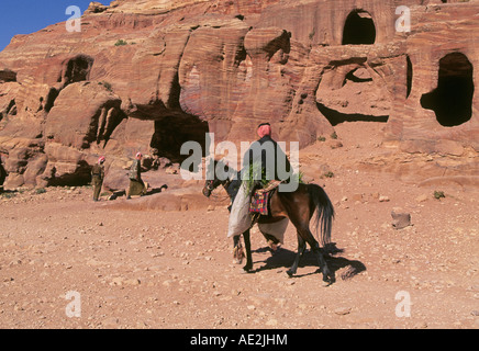 Un uomo arabo sulle passeggiate a cavallo attraverso le scogliere di arenaria nella zona intorno a Petra, Giordania. Foto Stock