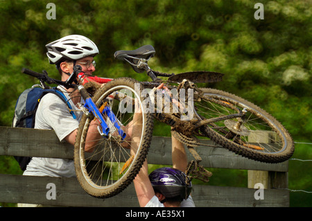 Gli amanti della mountain bike di spingere oltre il recinto in legno di Cotswold Hills Foto Stock