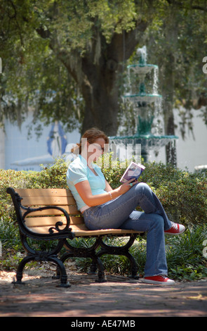 Donna con lo zenzero / capelli rossi lettura su una panchina nel parco in Lafayette Square vicino alla fontana a Savannah in Georgia negli Stati Uniti Foto Stock
