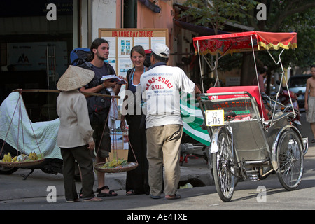 Venditore di frutta nel cappello conico e driver cyclo backpackers aiutano a trovare la loro strada il vecchio quartiere di Hanoi Vietnam Foto Stock