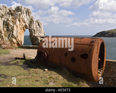 Rusty caldaia e roccia naturale arch a rovinato resti di Porth Wen laterizi sulla costa di Anglesey. Isola di Anglesey North Wales UK Foto Stock