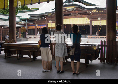 Tre donne pregando dopo l'offerta di monete presso la Meiji jingu sacrario scintoista di Tokyo Giappone Foto Stock