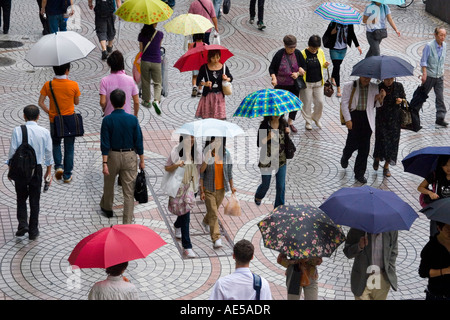 La gente che camminava su un marciapiede affollato ombrelli azienda sotto la pioggia al di fuori di Shinjuku stazione ferroviaria a Tokyo Giappone Foto Stock