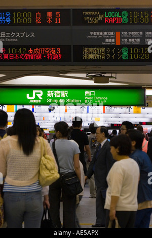 La gente camminare sotto i segni colorati che annuncia gli orari dei treni e le vie a Shinjuku stazione ferroviaria a Tokyo Giappone Foto Stock