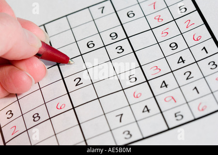 Mano che tiene una penna rossa per risolvere un sudoku numero giapponese puzzle Foto Stock