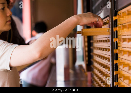 Donna giapponese di raggiungere nel cassetto di legno per tirare fuori il suo omikuji fortune - Sensoji tempio buddista Asakusa Tokyo Giappone Foto Stock