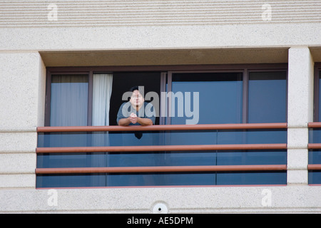 Americano cinese uomo età 40 appoggiata sulla ringhiera e guardando fuori da una stanza di un hotel balcone Foto Stock