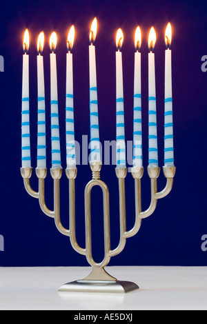 Un argento menorah ebraico con nove candele accese contro uno sfondo blu utilizzato al festival di Hanukkah Foto Stock