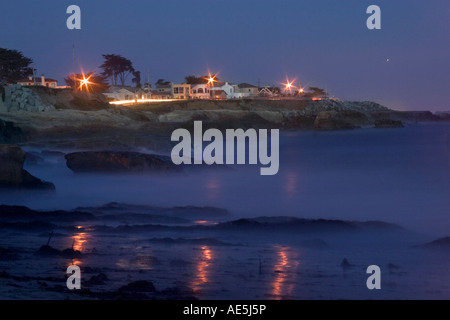 Misty cove lungo la fascia costiera sull'Oceano Pacifico durante la notte con le luci dalle case sopra riflettendo in sabbia Santa Cruz California Foto Stock