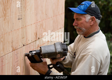 Carpenter mediante pistola sparachiodi per proteggere il legno compensato all esterno della casa per costruire la parete di taglio su una home SITO IN COSTRUZIONE Foto Stock