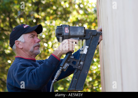 Carpenter mediante pistola sparachiodi per proteggere il legno compensato all esterno della casa per costruire la parete di taglio su una casa residenziale sito in costruzione Foto Stock