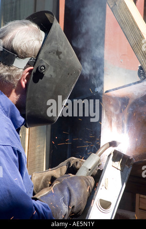 La formazione di scintille battenti come saldatore indossando maschera utilizza la torcia di saldatura per travi metalliche insieme Foto Stock