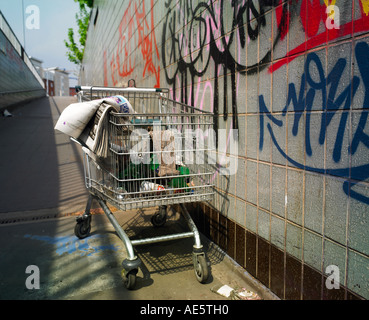 Carrello trolley utilizzato da persona senza dimora su un sottopassaggio di Manchester con graffitti sulla parete Foto Stock