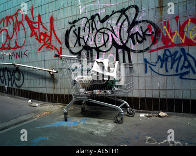 Carrello trolley utilizzato da persona senza dimora su un sottopassaggio di Manchester con graffitti sulla parete Foto Stock