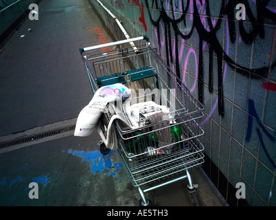 Carrello trolley utilizzato da persona senza dimora su un sottopassaggio di Manchester con graffitti sulla parete Foto Stock