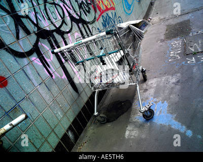 Carrello trolley utilizzato da persona senza dimora su un sottopassaggio di Manchester con graffitti sulla parete Foto Stock