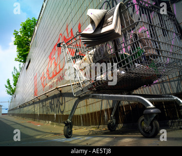 Carrello trolley utilizzato da persona senza dimora su un sottopassaggio di Manchester con graffitti sulla parete Foto Stock