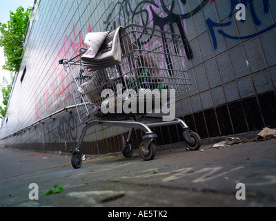 Carrello trolley utilizzato da persona senza dimora su un sottopassaggio di Manchester con graffitti sulla parete Foto Stock