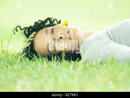 Donna sdraiata su erba con tarassaco in bocca Foto Stock