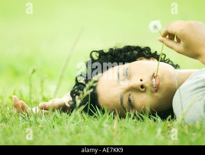 Donna sdraiata su erba con tarassaco in bocca Foto Stock