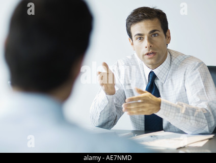 Imprenditore seduto alla scrivania che parla al secondo uomo Foto Stock