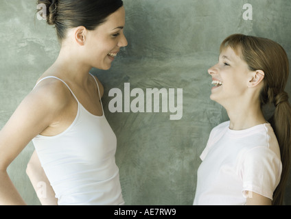 Due sorelle in piedi, guardando ogni altro e ridere, vista laterale Foto Stock