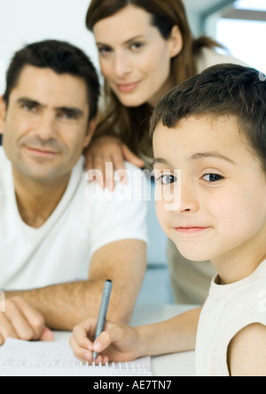 Ragazzo facendo compiti a casa con i genitori in background Foto Stock
