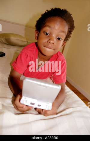 African American Black Boy in maglietta rossa la riproduzione di gameboy giovane ragazzo Foto Stock