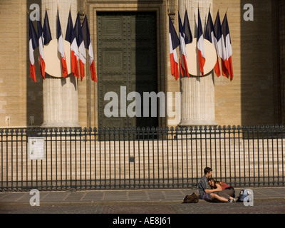 Giovane si siede sul terreno di fronte francese di tri-colore appeso bandiere dalle colonne del Pantheon Parigi Francia Foto Stock