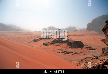 Rosso pavimento in sabbia del deserto con affioramenti rocciosi denominati Jebels nella distanza Wadi Rum Giordania Foto Stock