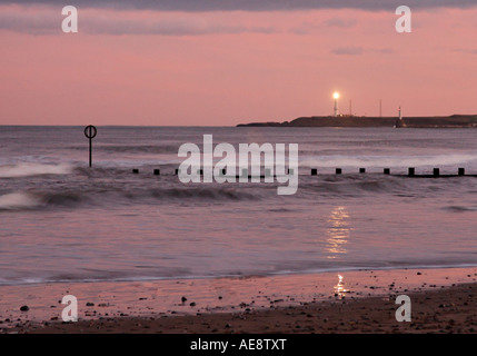 Onde si infrangono sulla riva davanti ad Aberdeen in Scozia con il faro in funzionamento. Foto Stock