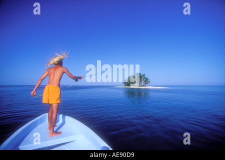 Uomo di Pesca a Mosca Report di Pesca fuori prua della barca con una piccola isola a distanza in Belize Caraibi modello e Proprietà immagine rilasciata Foto Stock