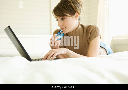 Giovane donna giaceva sul letto, utilizzando il computer portatile, tenendo carta di credito Foto Stock