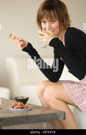 Giovane donna con aperitivo nel salotto, guardando la telecamera Foto Stock