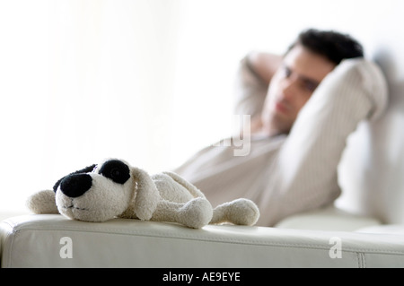 Pensare uomo seduto su un divano, cane di peluche in primo piano Foto Stock