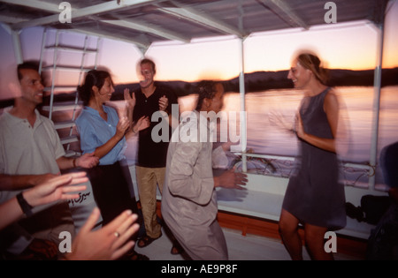 I turisti occidentali ballare con Nubian sailor su un tramonto crociera in barca lungo il fiume Nilo, Aswan, Egitto Foto Stock