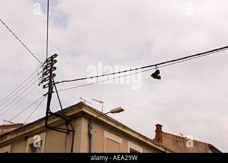 Un paio di scarpe pende dai suoi lacci da linee telefoniche in una città Foto Stock