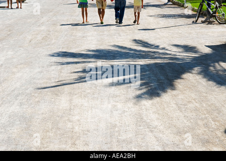 Una vista ritagliata di quattro gambe di popoli a piedi da spettatore lungo una soleggiata promenade Foto Stock