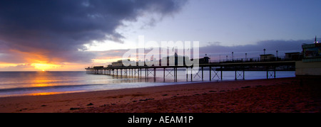 Alba sul foreshore a Paignton Devon meridionale con il molo vittoriano in background e il sorgere del sole in un cielo nuvoloso Foto Stock