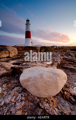 Portland Bill lighthouse appena prima dell'alba con una grande pietra di Portland boulder in appoggio sulla sommità di una rupe in primo piano Foto Stock