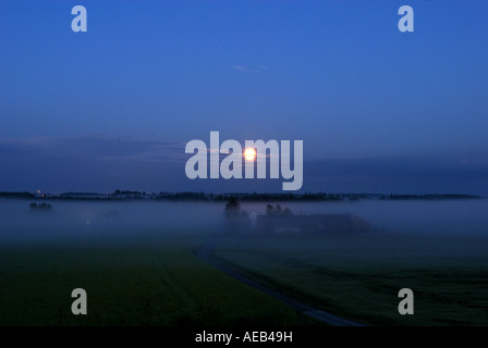 Un tappeto di nebbia nebbia giace al di sopra di un campo molto vasto che circondano la fattoria al centro del telaio Foto Stock