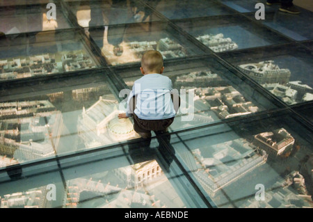 Giovane ragazzo rannicchiato e guardando attraverso un pavimento di vetro a un modello in scala piano per l opera del Musee D'Orsay a Parigi Francia Foto Stock
