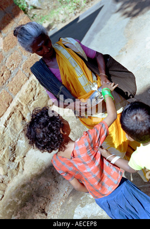 Una vecchia signora vestita di saree accetta bracci da due bambini, Kerala, India Foto Stock